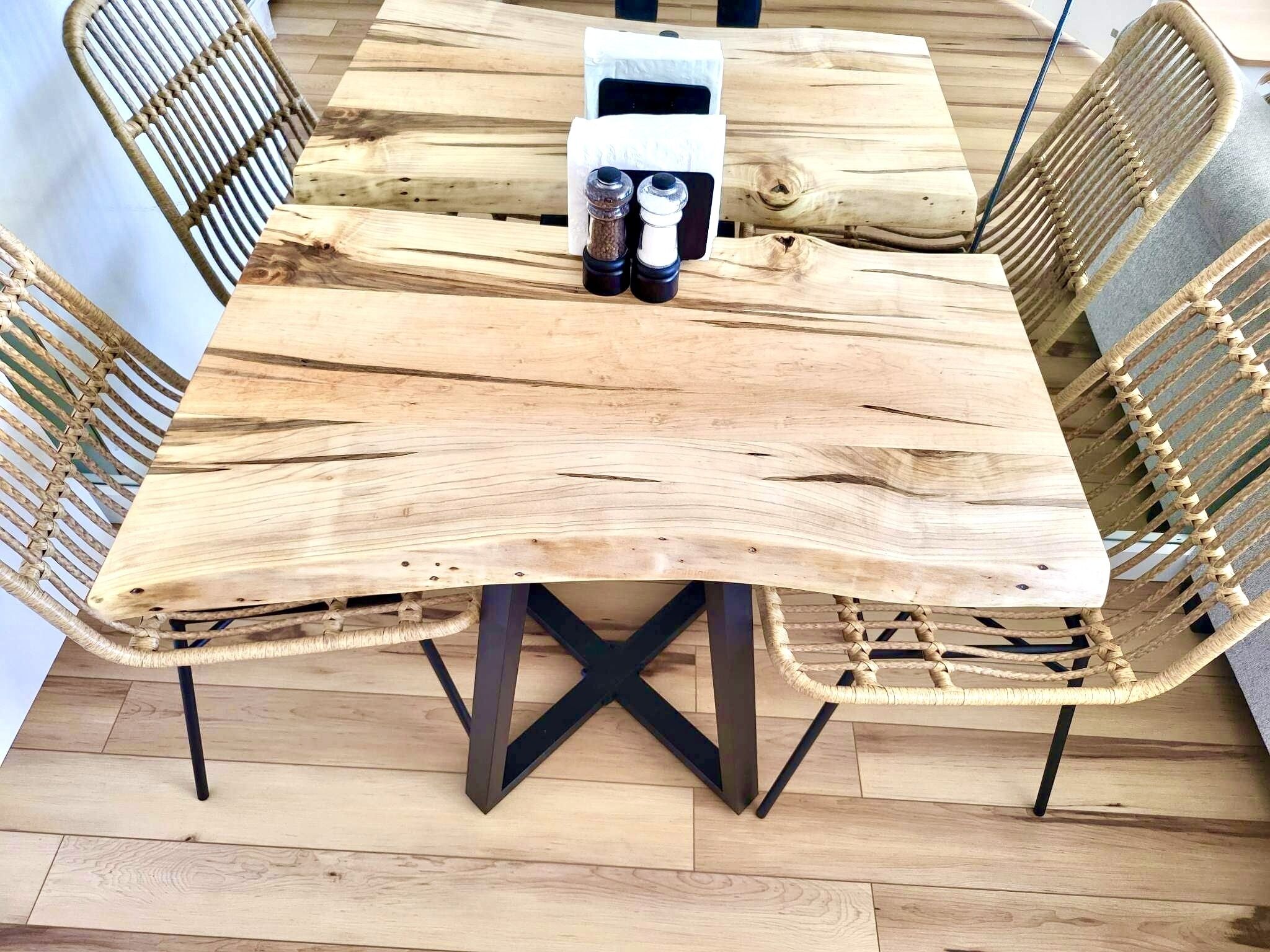 A rustic wooden dining table with a natural wood grain finish, surrounded by woven rattan chairs with black metal legs.