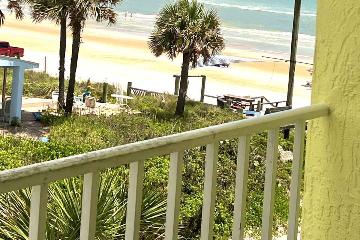 A beach view from a balcony with palm trees, a sandy beach, and the ocean.