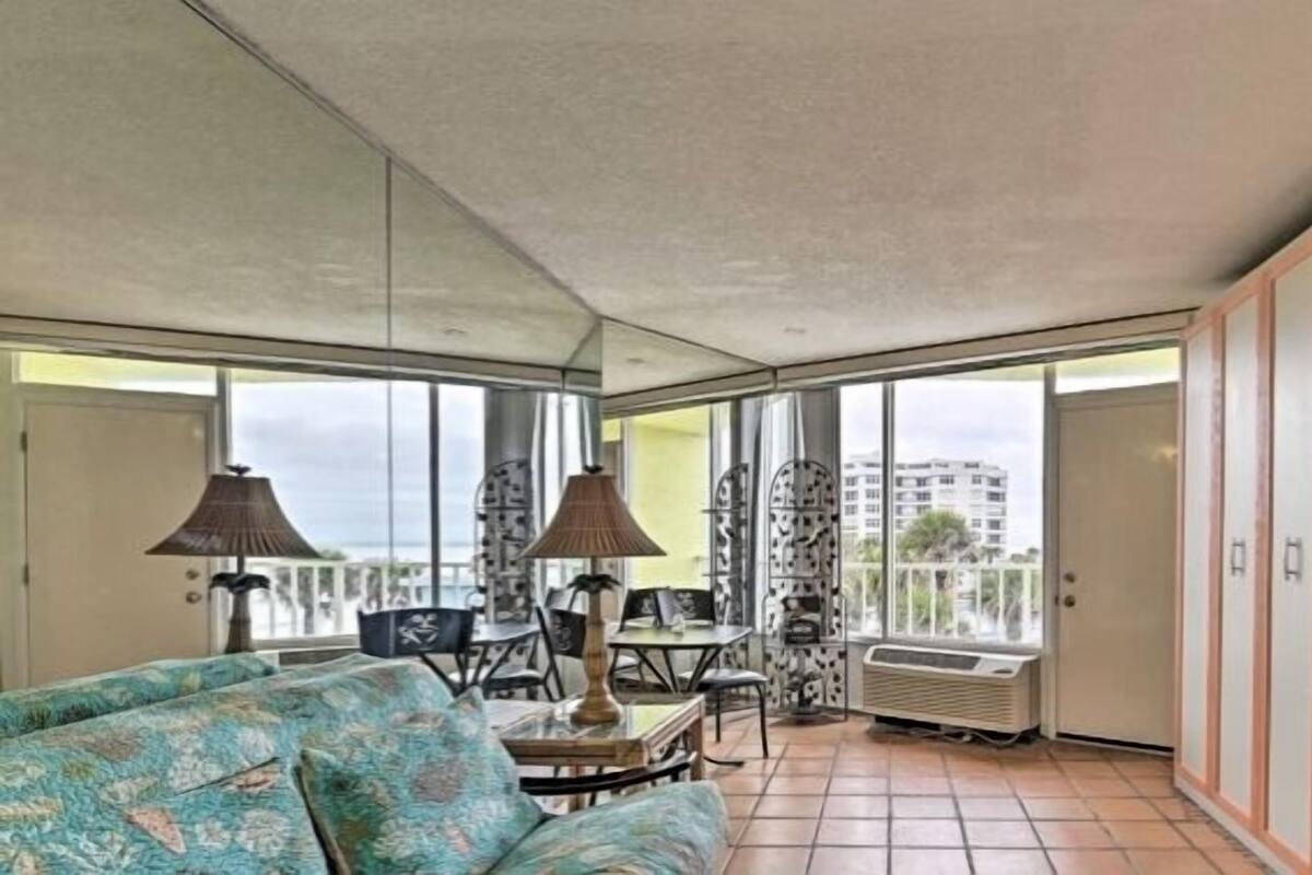 A spacious living room with a large window, a sofa, a table with lamps, and a wardrobe.