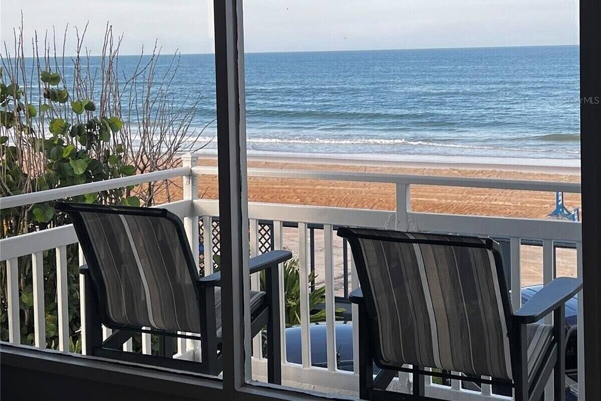 A covered outdoor area with two chairs and a view of the beach.