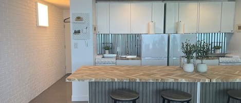 A modern kitchen with white cabinets, a wooden island with stools, and a striped backsplash.
