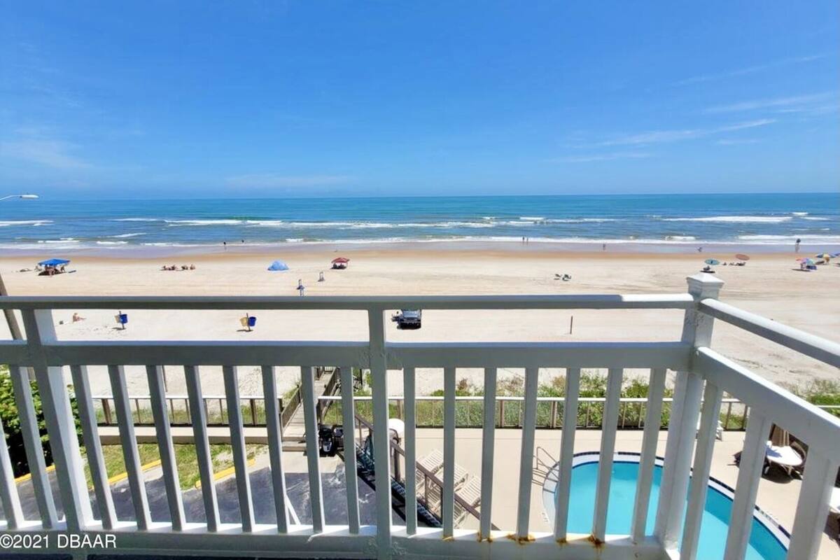 A beach view from a balcony with a pool and lounge chairs.