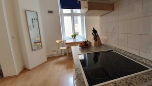 A modern kitchen with a black induction cooktop, a wooden chair, and a window with a view of the outside.