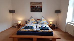 A double bed with geometric patterned pillows, bedside lamps, and a wall-mounted artwork.