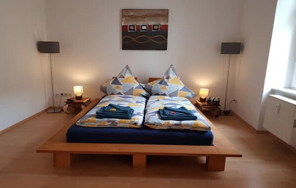 A double bed with geometric patterned pillows, bedside lamps, and a wall-mounted artwork.