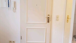 A closed white door with a double-panel design, a wall-mounted light switch, and a power outlet on the left.