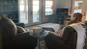 Een woonkamer met een bank, een glazen salontafel, een televisie en een plafondventilator.