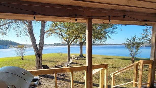 Een overdekt terras met uitzicht op een meer, een houten terras en een barbecue.