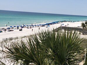 A beach with white sand, blue umbrellas, and people relaxing.