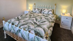 A bed with a leaf-patterned bedspread, a white headboard, and two bedside tables with lamps.