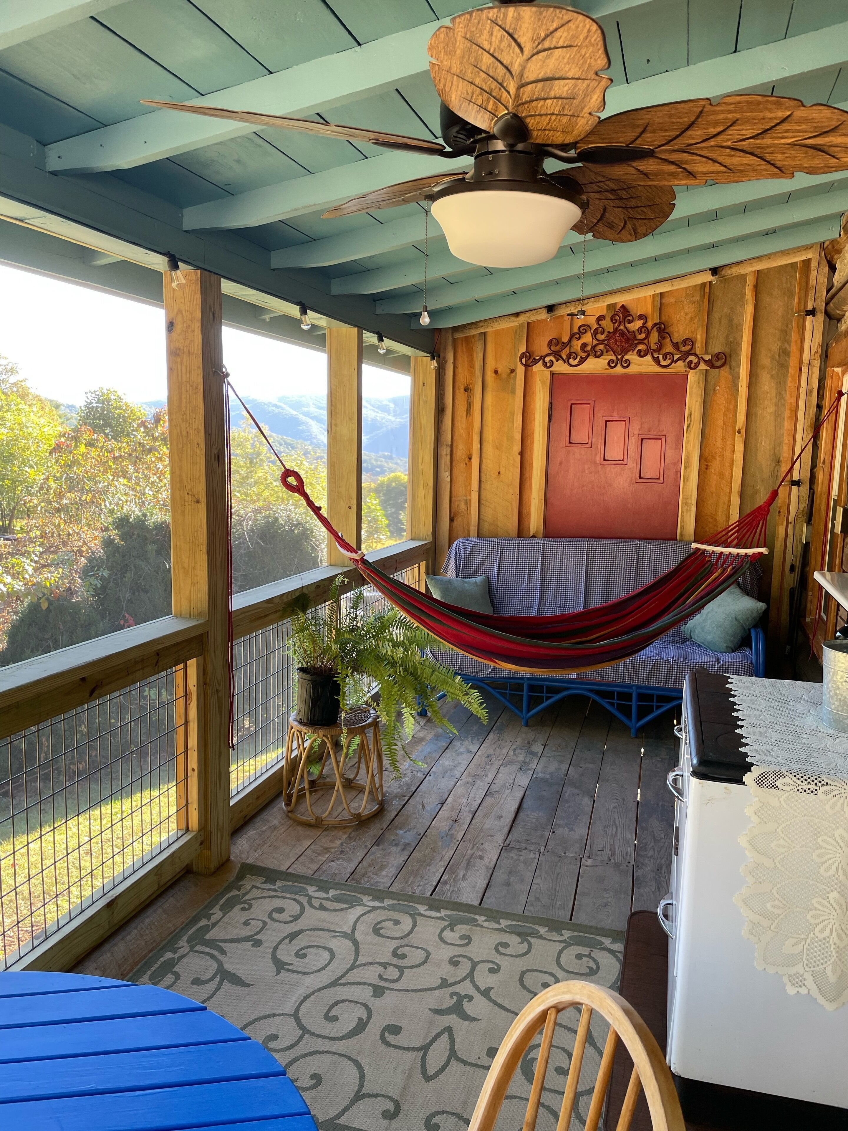 A wooden deck with a hammock, a bed with a checkered bedspread, and a view of the outdoors.