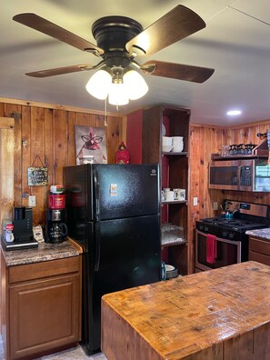 A kitchen with wooden paneling, a black refrigerator, a coffee maker, a stove, and a ceiling fan.