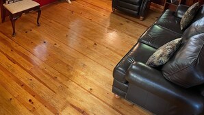 Ein gemütliches Wohnzimmer mit Holzböden, einer roten Tür, einem schwarzen Ledersofa, einem schwarzen Sessel, einem kleinen Tisch und einem Deckenventilator.