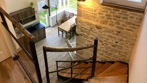 A staircase with a stone wall, a dining area with a table and chairs, and a kitchen with a sink and countertop. - Gîtes Onyx: l'Albizia, Lot - Vallée de la Dordogne (Bétaille)
