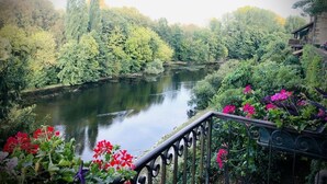 A riverside view with a balcony railing, lush greenery, and a calm river. - Gîtes Onyx: l'Albizia, Lot - Vallée de la Dordogne (Bétaille)