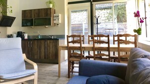 A modern kitchen with wooden cabinets, a built-in oven, and a coffee machine. There is a dining area with a wooden table and chairs, and a sofa. - Gîtes Onyx: l'Albizia, Lot - Vallée de la Dordogne (Bétaille)
