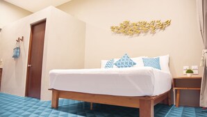 A hotel room with a wooden bed, a geometric patterned floor, a wall-mounted decorative piece, and a small bedside table with a plant.