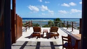 A terrace with wooden furniture and a view of the ocean.