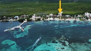 An aerial view of a coastal area with a pier, boats, and a hotel with a large building highlighted by a yellow arrow.