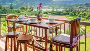 A wooden dining table set with plates, glasses, and a potted orchid, overlooking a mountainous landscape. - (4323) 1 Br Hanalei Bay Resort, Ocean view and Plenty of Amenities (Princeville)