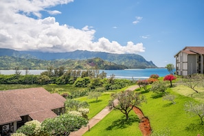 Um jardim exuberante com um caminho que leva a um edifício com telhado vermelho, com vista para um lago e montanhas.