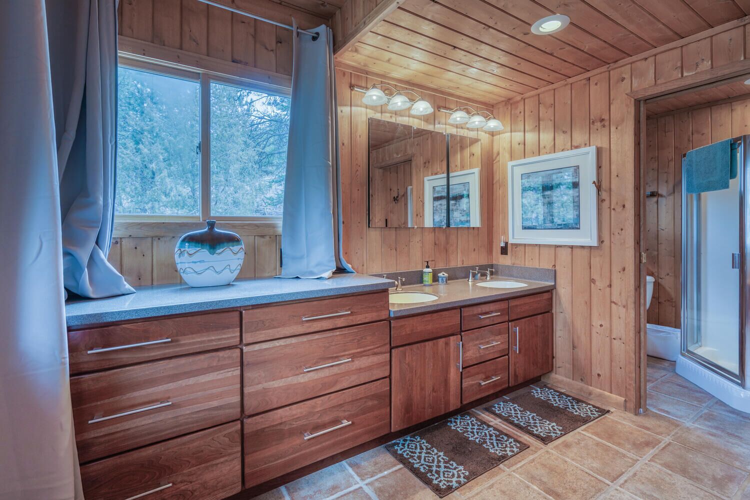 Une salle de bain rustique, aménagée dans une cabane en bois, avec une grande fenêtre, un lavabo et un miroir.
