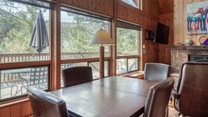 Interior de una cabaña de madera con una mesa de comedor, sillas, una lámpara y una chimenea.