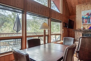 A wooden cabin interior with a dining table, chairs, a lamp, and a fireplace.