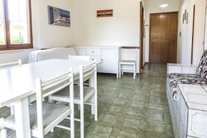 A room with a dining table, chairs, a sofa, a kitchenette, and a door.