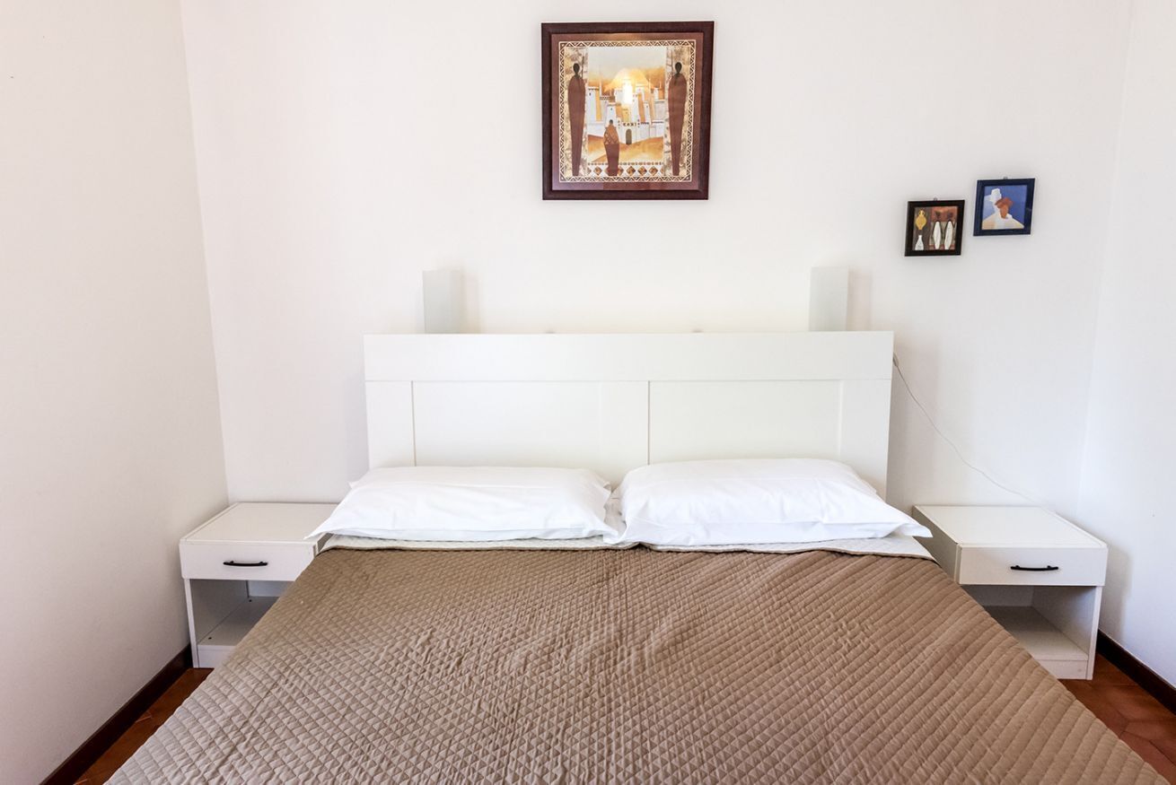 Un letto con una testiera bianca, due comodini, una coperta trapuntata marrone e un quadro incorniciato sopra il letto.