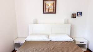 Ein Bett mit weißem Kopfteil, zwei Nachttische, einer braunen gesteppten Tagesdecke und einem gerahmten Bild darüber.