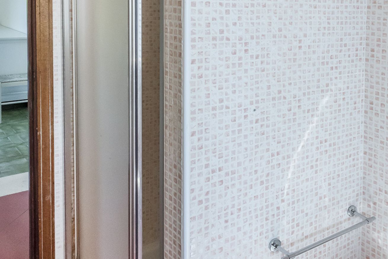 Bagno con parete piastrellata, porta in vetro e porta asciugamani in metallo.
