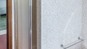 Ein Badezimmer mit gefliesten Wänden, einer Glastür und einem Metallhandtuchhalter.