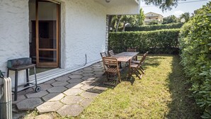 Eine Terrasse mit Tisch und Stühlen, eine Glastür und ein Steinweg, der zu einem Haus führt.