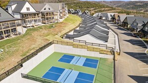 Ein Tennisplatz mit umgebendem Zaun, neben einer Reihe von Häusern mit geneigten Dächern.