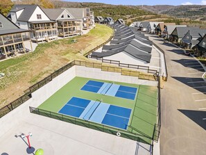 A tennis court with a surrounding fence, adjacent to a row of houses with sloped roofs. - Enjoy Arcade Games! Ski Ball, Shuffleboard, Air Hockey, Dart Board, Hot Tub & Cmty Pools (Hollister)