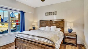 Ein Schlafzimmer mit einem hölzernen Bett, zwei Nachttischen, einem Deckenventilator und einem großen Fenster mit Blick auf einen Spielplatz.