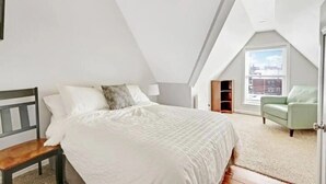 Un dormitorio con cama, una silla y ventana.