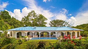 Una casa amb piscina, envoltada de vegetació exuberant i plantes tropicals.