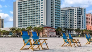 Un hotel frente a la playa con varios edificios de gran altura, sillas de playa y palmeras.