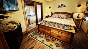 Une chambre à coucher avec un lit en bois, deux lampes de chevet, une télévision, une commode en bois et une porte donnant sur un balcon.