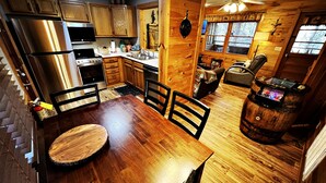 L’intérieur d’un chalet en bois comprend une table à manger, des chaises, une cuisine équipée d’appareils électroménagers en acier inoxydable, une cheminée et un tonneau.