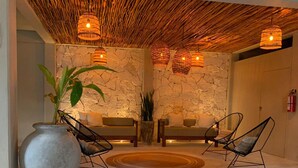 A lobby with a stone wall, two sofas, a large vase, and wicker chairs. - Beachfront 1BR Apartment w/ Terrace & Beach Club (Mahahual)