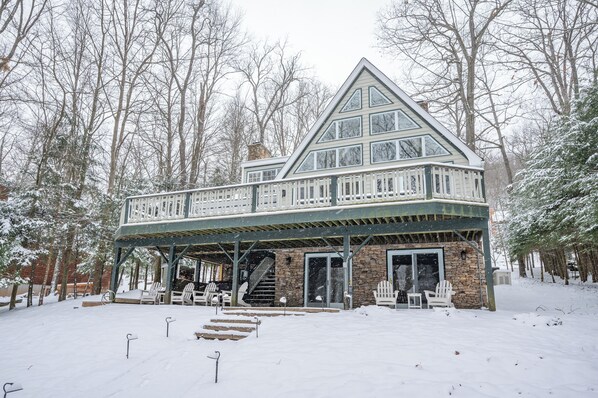A lodge with a stone facade, a balcony with Adirondack chairs, and a staircase leading to the entrance. - Lakefront Luxury w/ Fireplaces, Hot Tub & Dock (McHenry)