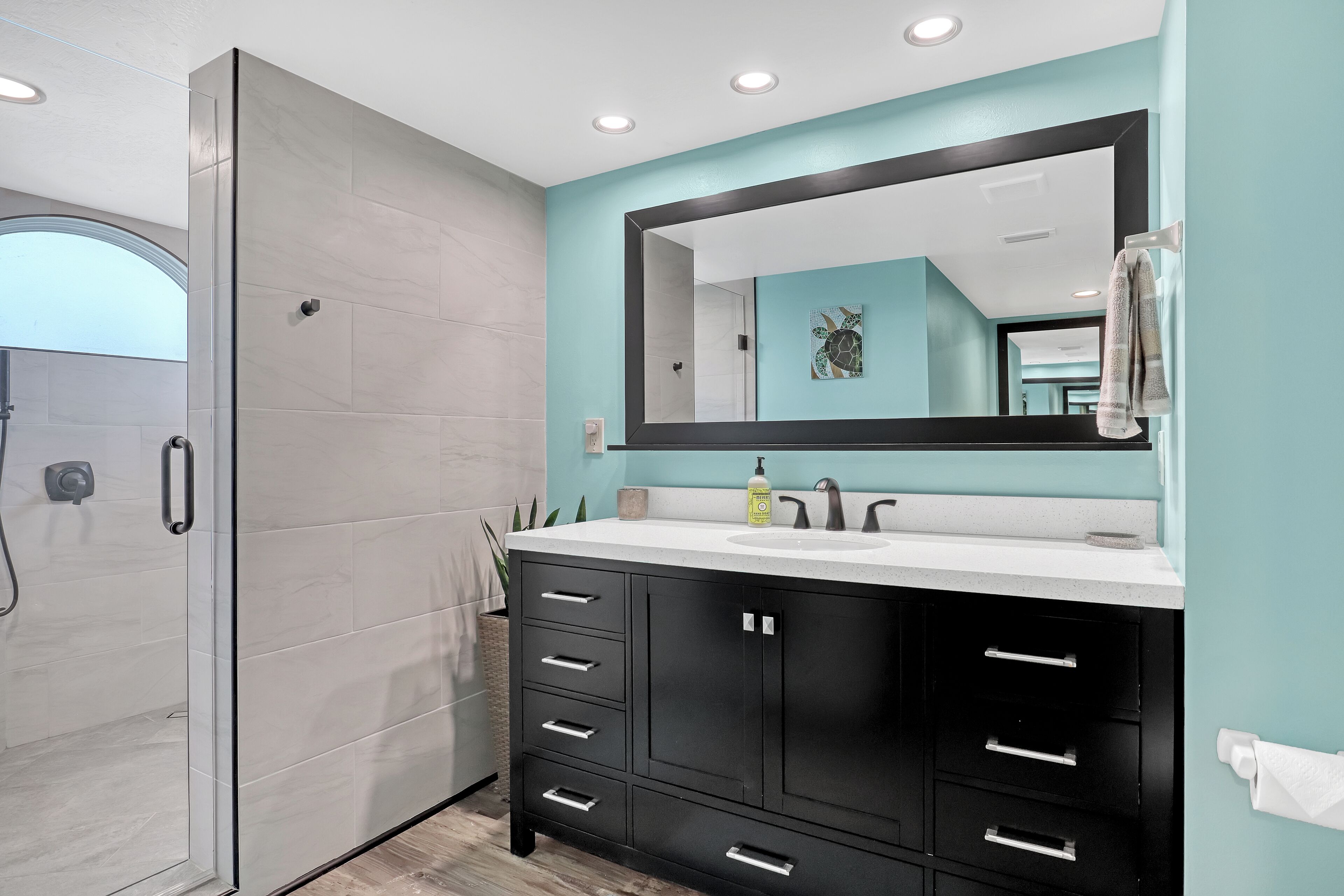 Un baño moderno con cabina de ducha de vidrio, un espejo grande y un mueble de tocador negro con varios cajones.