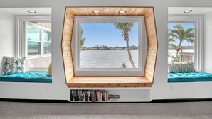 Une pièce dotée d’une grande fenêtre donnant sur un plan d’eau, de bibliothèques intégrées et de poutres en bois apparentes au plafond.