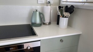 A kitchen with a black induction cooktop, a green kettle, a white paper towel holder, and a utensil holder.