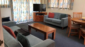 A living room with a grey sofa, a wooden coffee table, a television on a wooden stand, and a floral curtain.