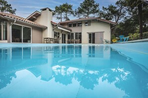 Ein Swimmingpool mit freiem Blick auf ein Haus mit einem geziegelten Dach und großen Fenstern.