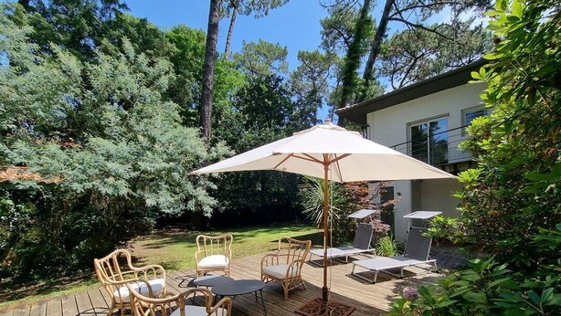 A wooden deck with wicker furniture and a large umbrella. - Attractive family home for 10 people in popular Hossegor lake district (SOORTS HOSSEGOR)